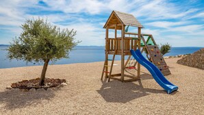 A wooden play structure with a slide on a pebbled beach with a clear view of the sea. - Lovely home in Kosljun (Kosljun)