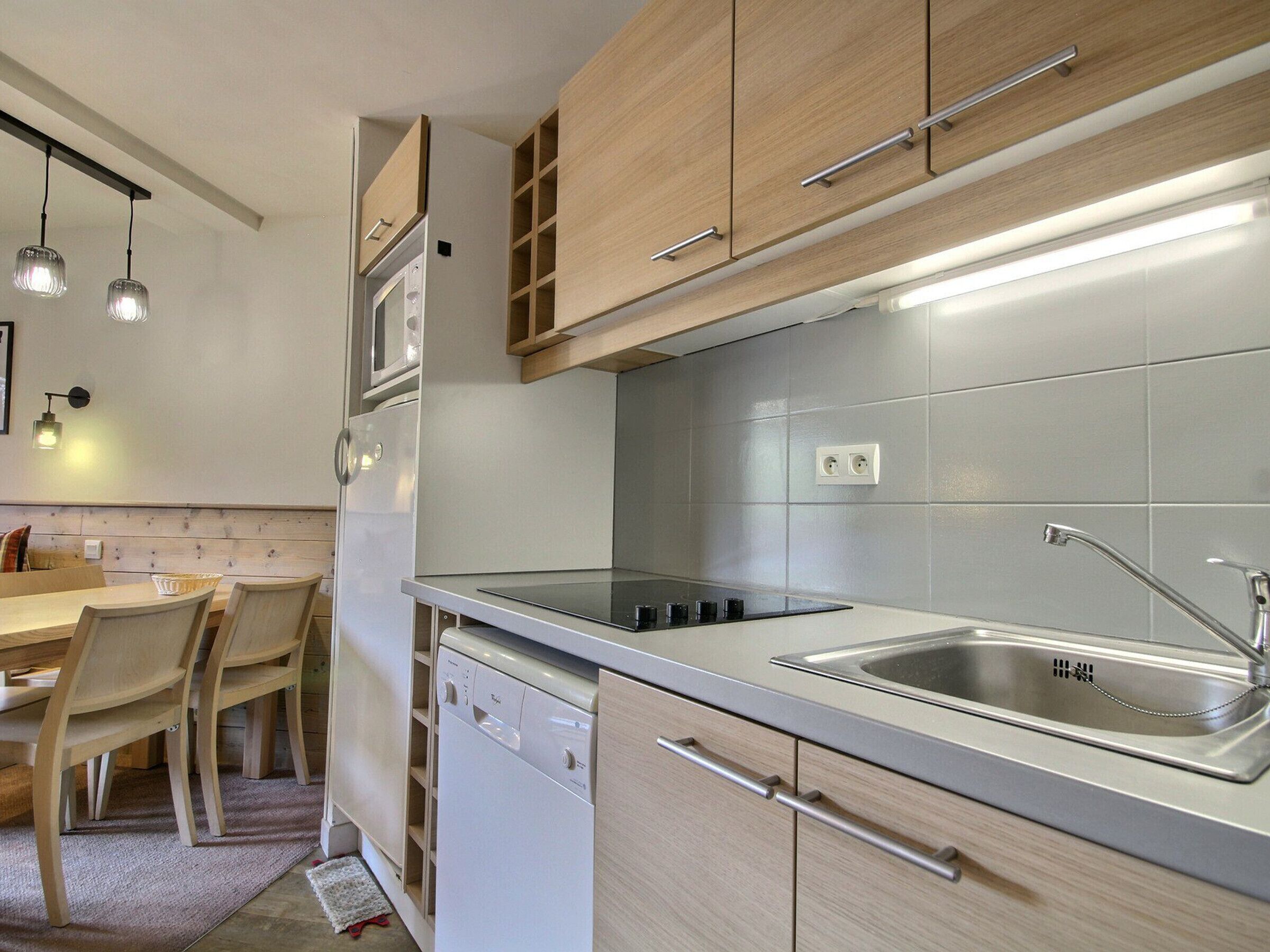 Una cucina moderna con mobili in legno, lavastoviglie integrata, lavello in acciaio inossidabile e illuminazione a sospensione.