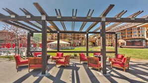 Un patio al aire libre con pérgola de madera, sillas rojas con cojines y mesas.