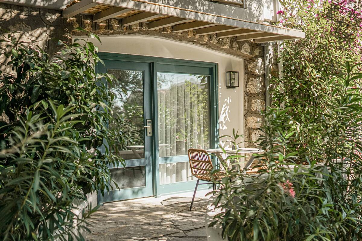 A stone building with a curved entrance, a wooden chair, and potted plants.