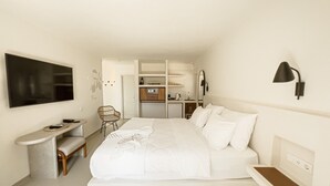 Un dormitorio con cama, mesita de noche, silla, televisor y una zona de kitchenette.