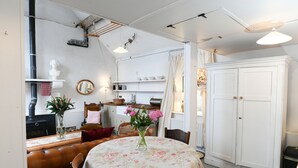 Een eetruimte met een ronde tafel, stoelen en een vaas met bloemen. Er is een witte kast en een raam met gordijnen.