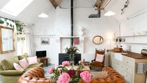 Een gezellige woonkamer met een groene bank, een bruin leren poef en een eettafel met roze bloemen.