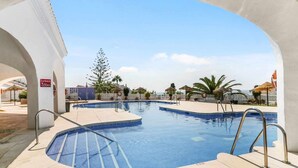 A swimming pool with a tiled deck, metal handrails, and a clear blue sky. - Capistrano Playa 618 (Nerja)