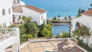 A courtyard with a pool, surrounded by white buildings with red-tiled roofs, overlooking a beach. - Capistrano Playa 618 (Nerja)