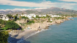 A coastal town with white buildings, a sandy beach, and rocky cliffs. - Capistrano Playa 618 (Nerja)