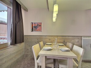 A dining area with a wooden table set for four, a vase, and a framed picture on the wall.