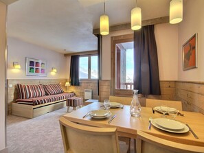A cozy room with a wooden bed, a dining table set for two, and a view of the outdoors.