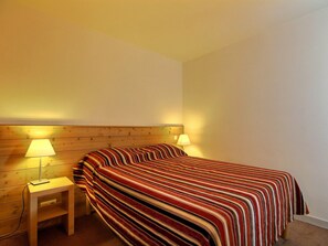 A hotel room with a wooden headboard, a single bed with a striped bedspread, two bedside lamps, and a small wooden nightstand with a lamp.