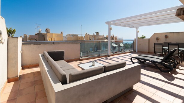 Eine Dachterrasse mit einer eingebauten Sitzecke, einem kleinen Tisch und einem Grillbereich.