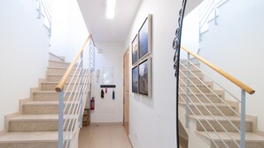 Eine Treppe mit beigen Stufen und weißen Geländern, die zu einem Zwischenpodest mit einem Feuerlöscher und einer Tür führt.
