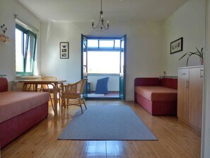 Una sala de estar acogedora con piso de madera, una mesa de comedor con sillas, un sofá rojo, un sofá azul, un armario pequeño y un ventanal con vistas.