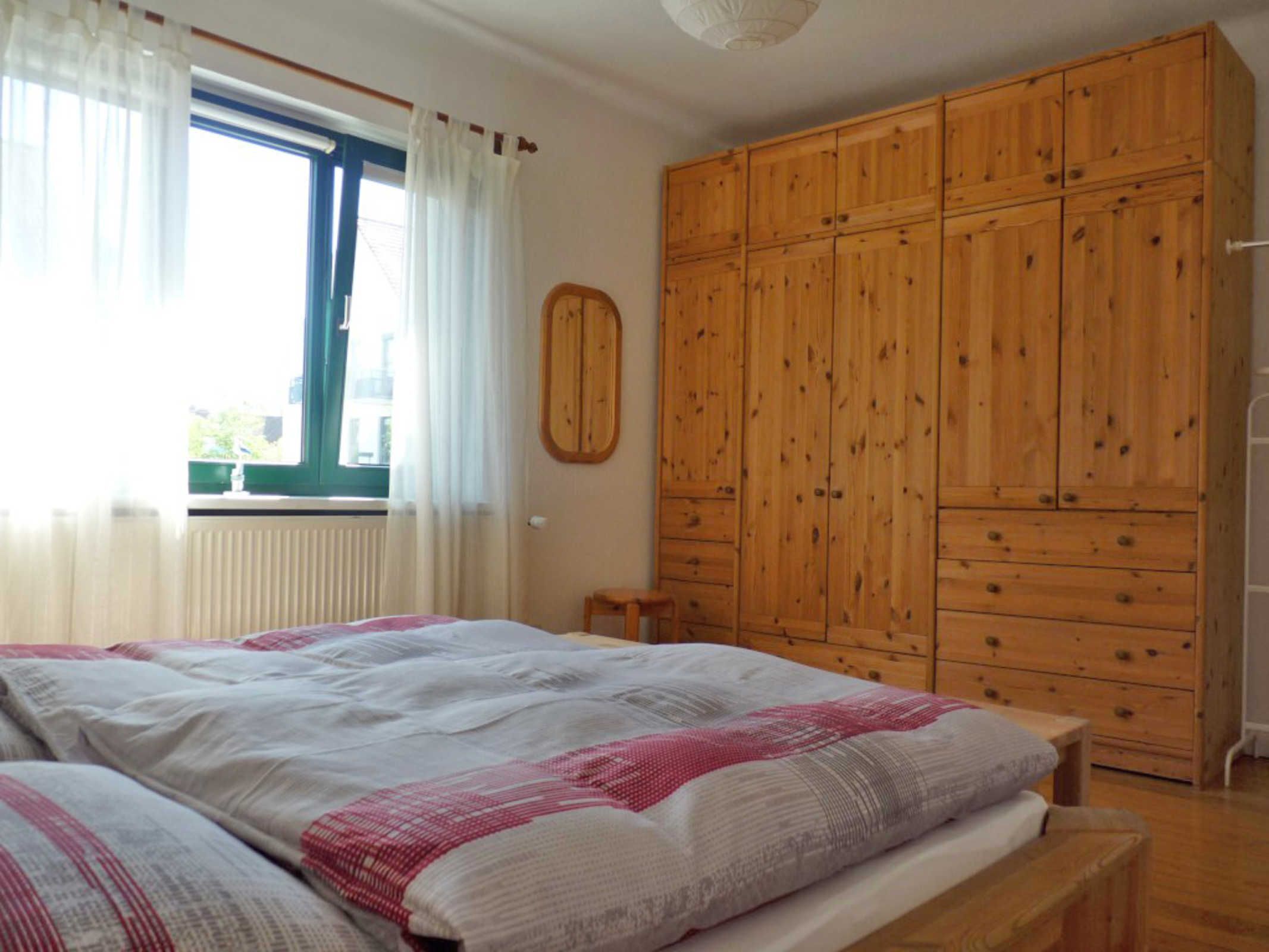 Quarto com cama grande, guarda-roupa de madeira e janela com cortinas.