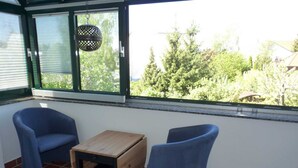 A room with two blue chairs, a small wooden table, and a view of trees through a large window. - Apartment Silbermöwe Object-ID 121011 (Waren (Müritz))