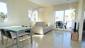 A spacious living area with a glass dining table, a sofa, and a balcony with outdoor furniture.
