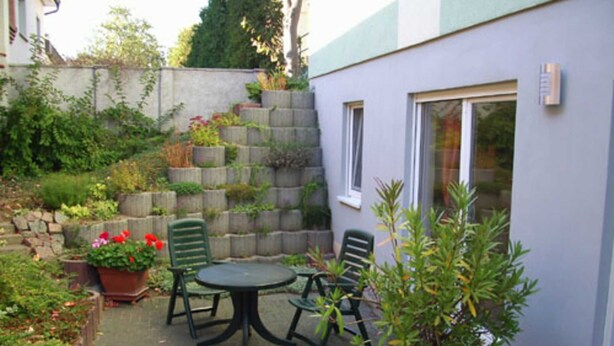 A patio with a table and chairs, surrounded by potted plants and a stone wall. - Apartment on Gregoriusberg Object-ID 121158 (Waren (Müritz))