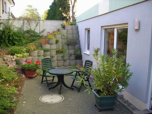 Eine Terrasse mit Tisch und Stühlen, umgeben von Topfpflanzen und einer Steinmauer.