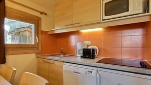 A compact kitchen with wooden cabinets, a microwave, a coffee maker, and a dishwasher. - Lovely studio cabin for 4 people, near slopes (Belle Plagne)