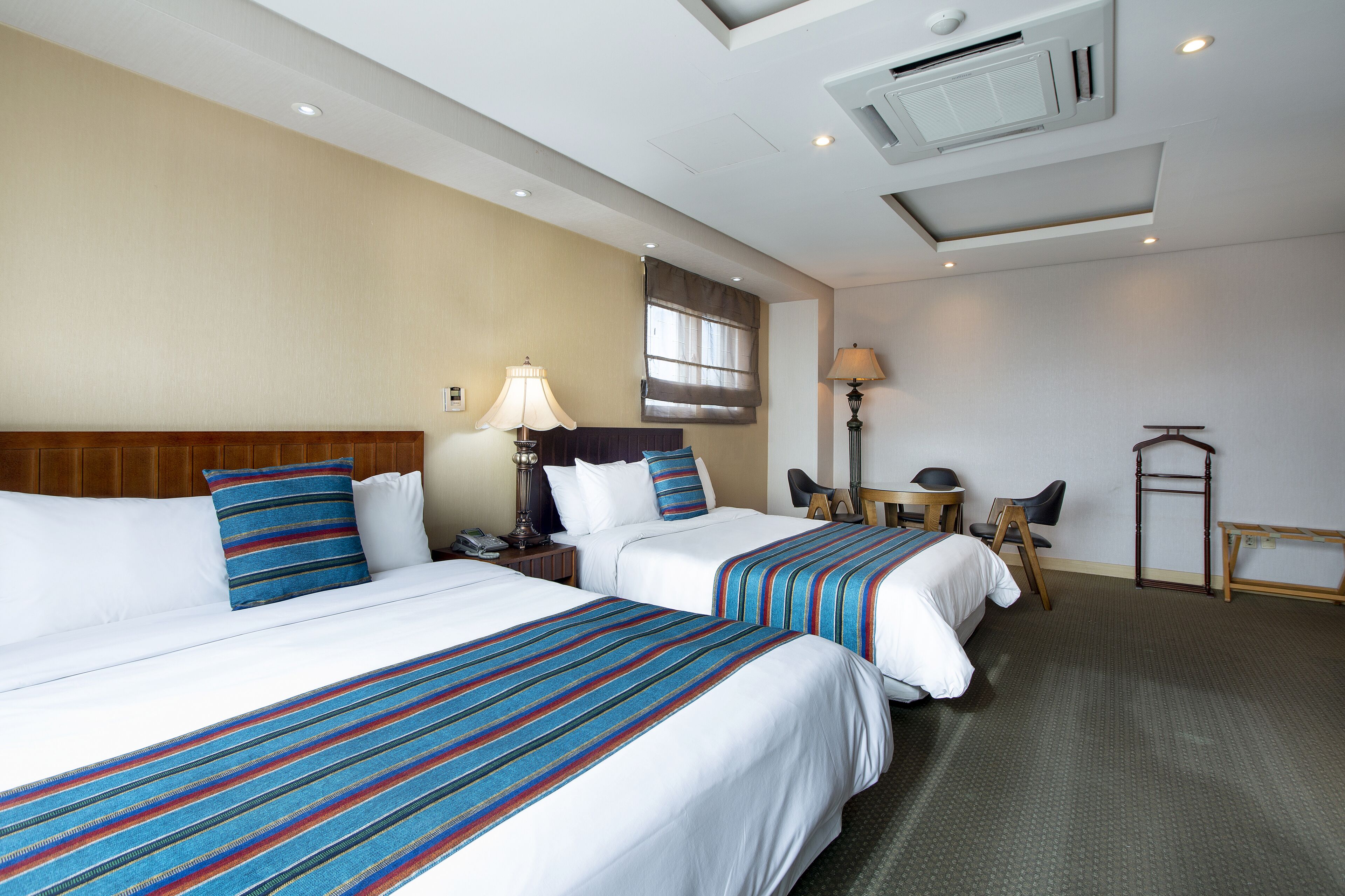 A hotel room with two beds, a desk, a chair, and a lamp.