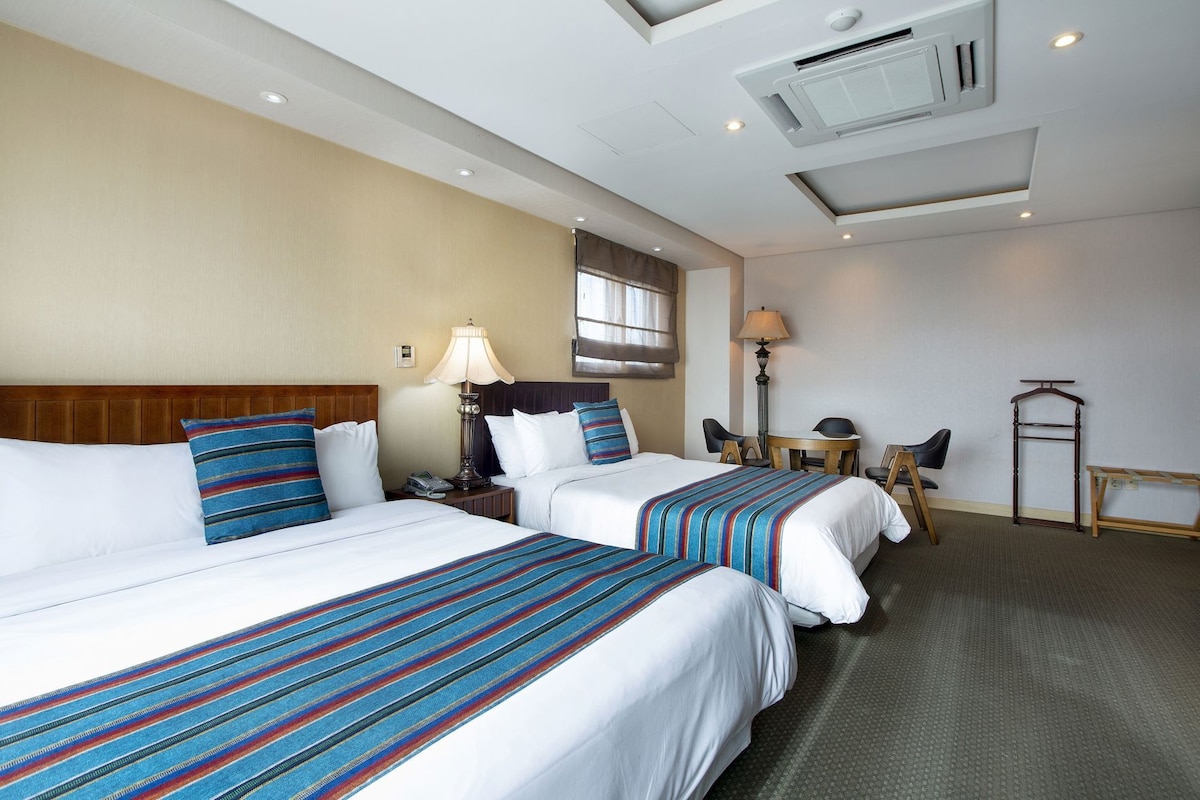 Habitación de hotel con dos camas, un escritorio, una silla, una lámpara y una lámpara colgante.