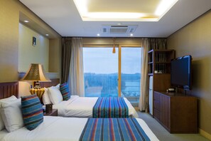 A hotel room with two beds, a television, a bookshelf, and a large window with a view.