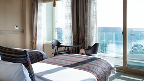 A hotel room with a bed, two chairs, a small table, and a large window with a view of a cityscape. - Ritz Plaza Hotel (Gunsan)