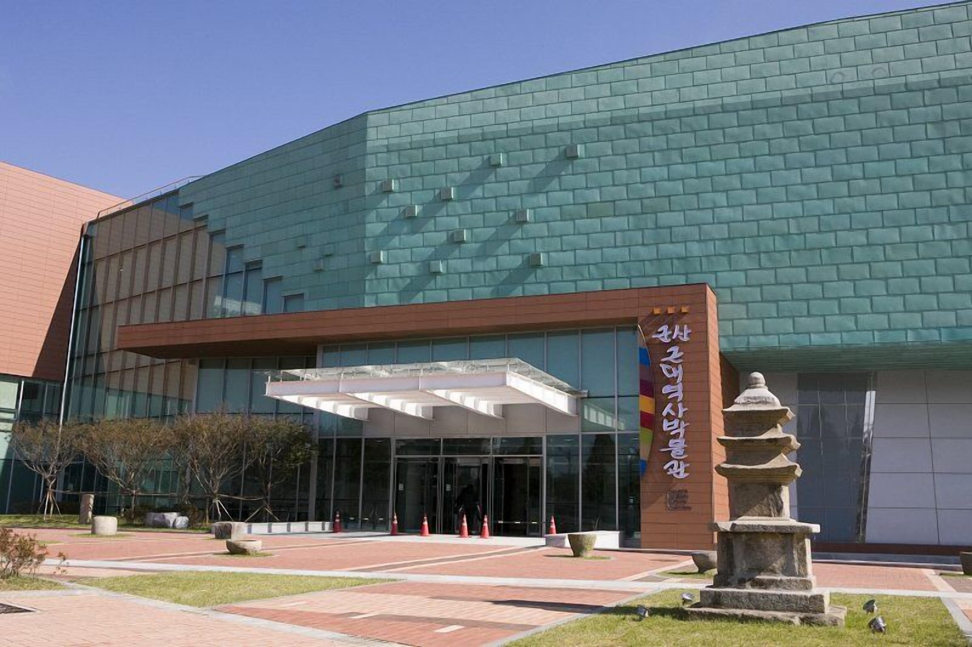 Un edificio moderno con fachada de vidrio y un monumento de piedra en primer plano.