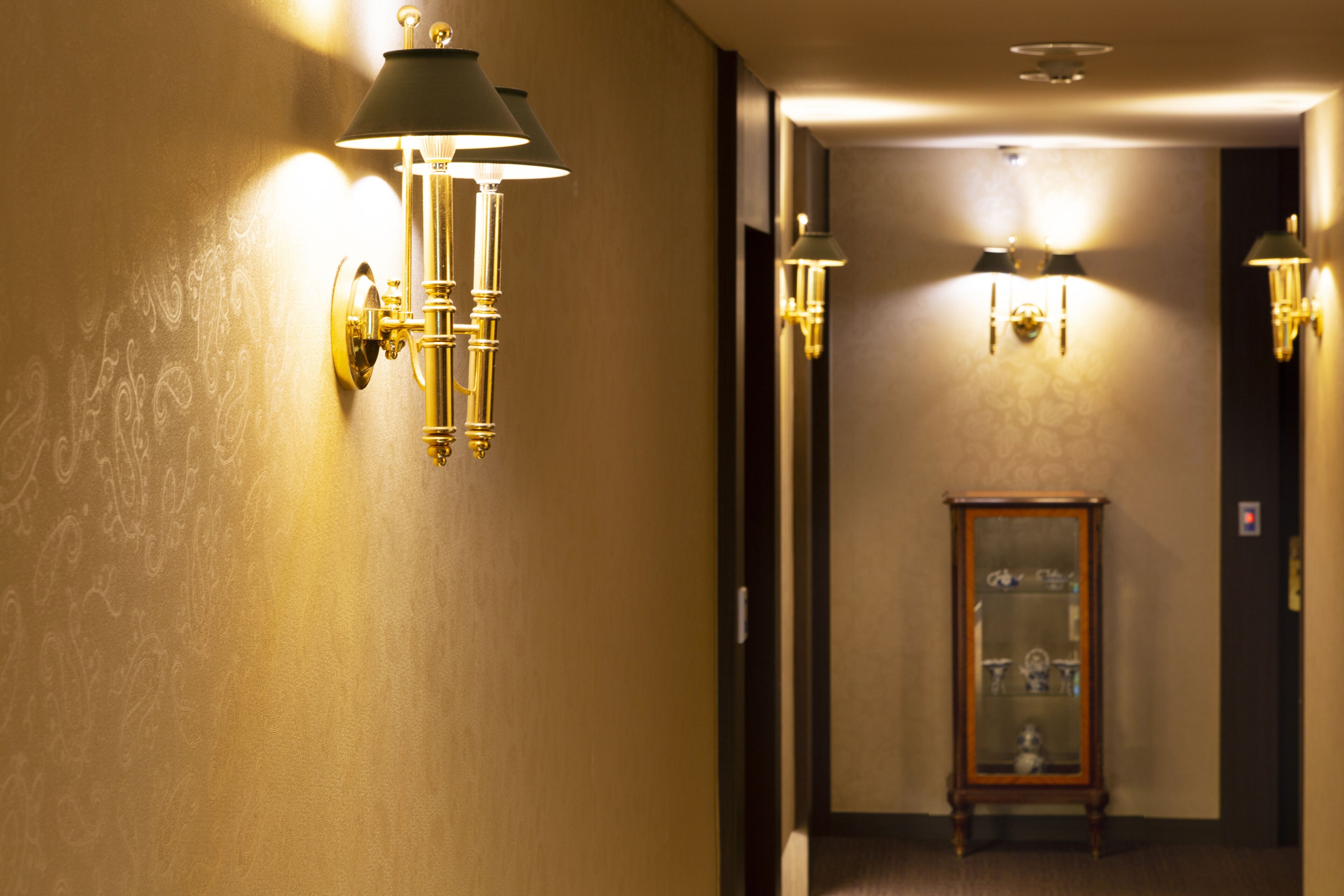 A hallway with wall-mounted sconces and a display cabinet.
