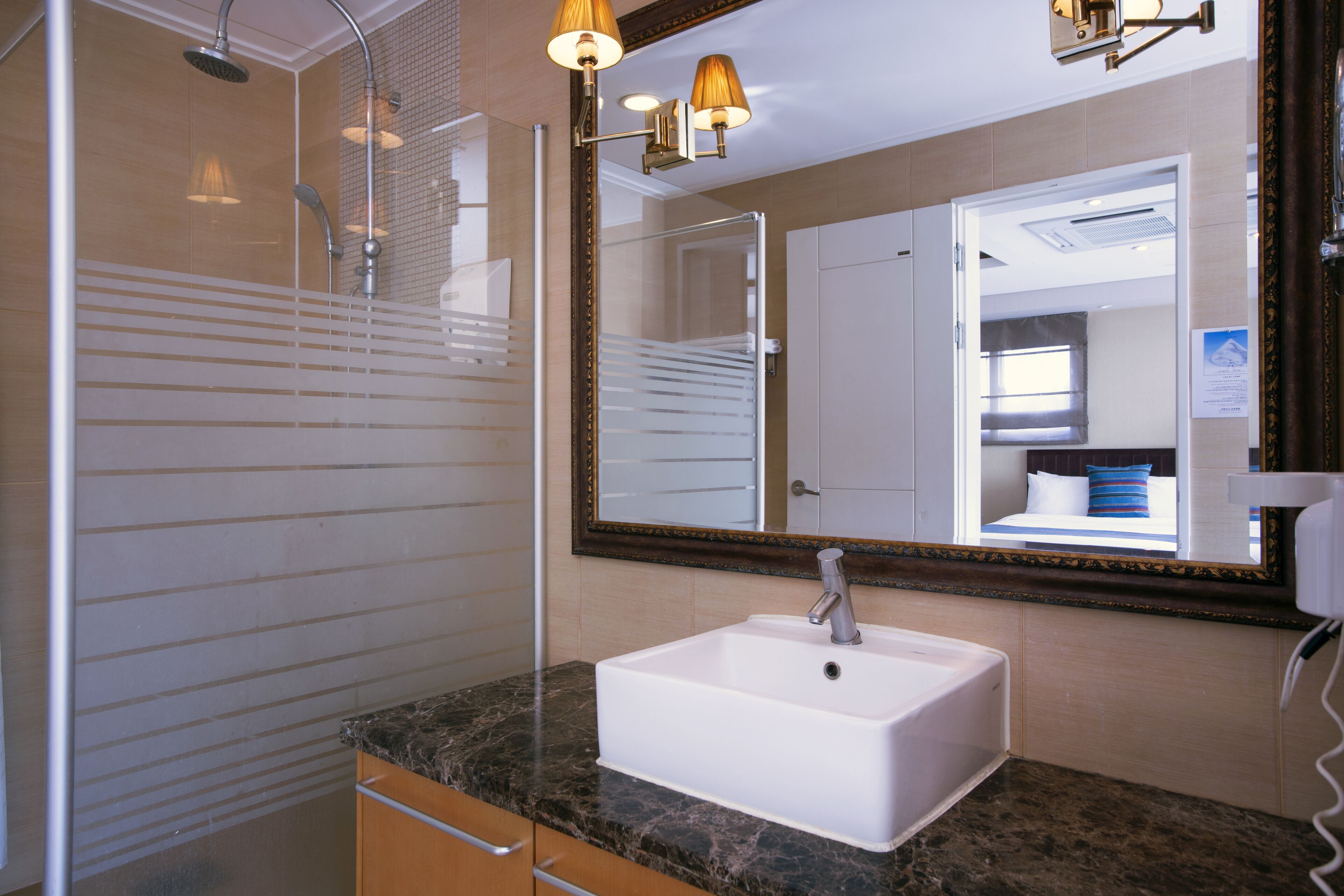 A bathroom with a white sink, a shower, and a large mirror with a wooden frame.