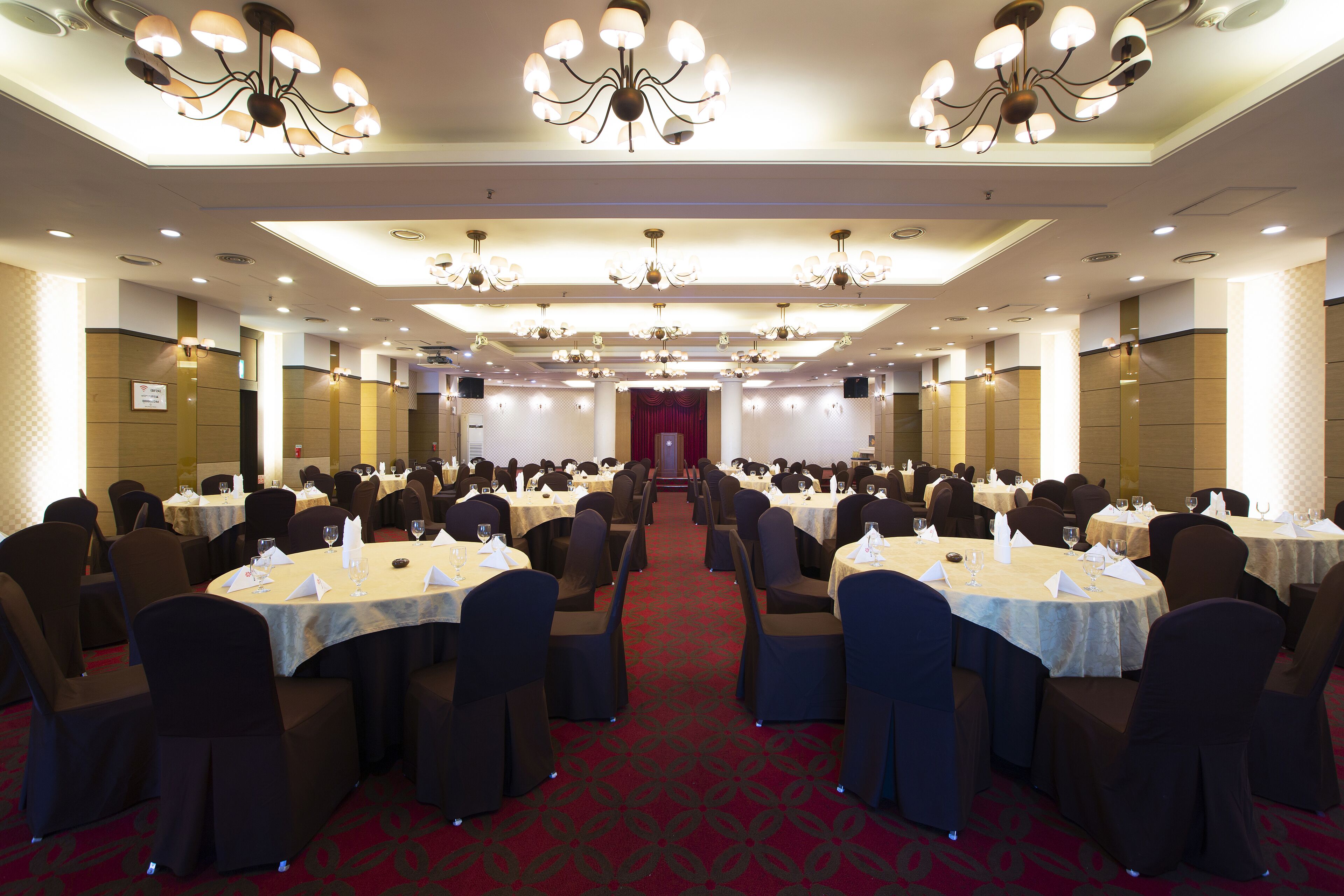 A banquet hall with multiple round tables, chairs, and chandeliers.