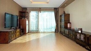 A spacious room with a large flat-screen TV, wooden furniture, and a large window with sheer curtains. - Ritz Plaza Hotel (Gunsan)
