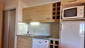 A compact kitchen with wooden cabinets, a microwave, a dishwasher, and a marble backsplash.