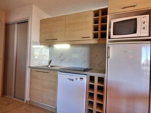 Uma cozinha compacta com armários de madeira, micro-ondas, lava-louças e painel de fundo de mármore.