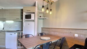 A compact kitchen with a microwave, refrigerator, and dishwasher. There is a wooden dining table with chairs and a bench.