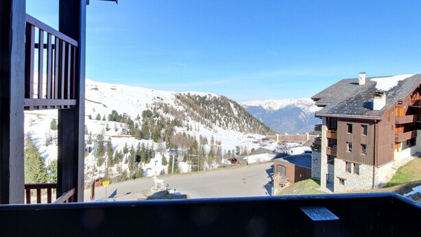 A mountain view with a wooden building, a paved area, and snow-covered slopes.