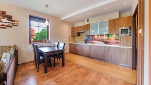 A modern kitchen with wooden cabinets, a dining table, and a window with a view of greenery.