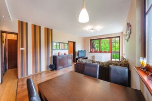 A modern dining area with a wooden table and chairs, a television, and a sofa with patterned cushions. - Sun & Snow Willa Hania (Krynica Morska)