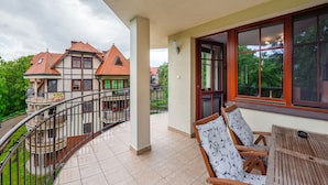 A balcony with a wooden table and chairs, a view of neighboring houses, and a railing.