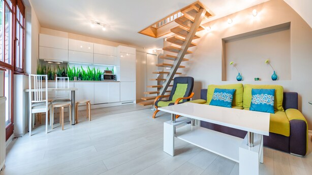 A modern living room with a staircase, a dining area, and a kitchen.