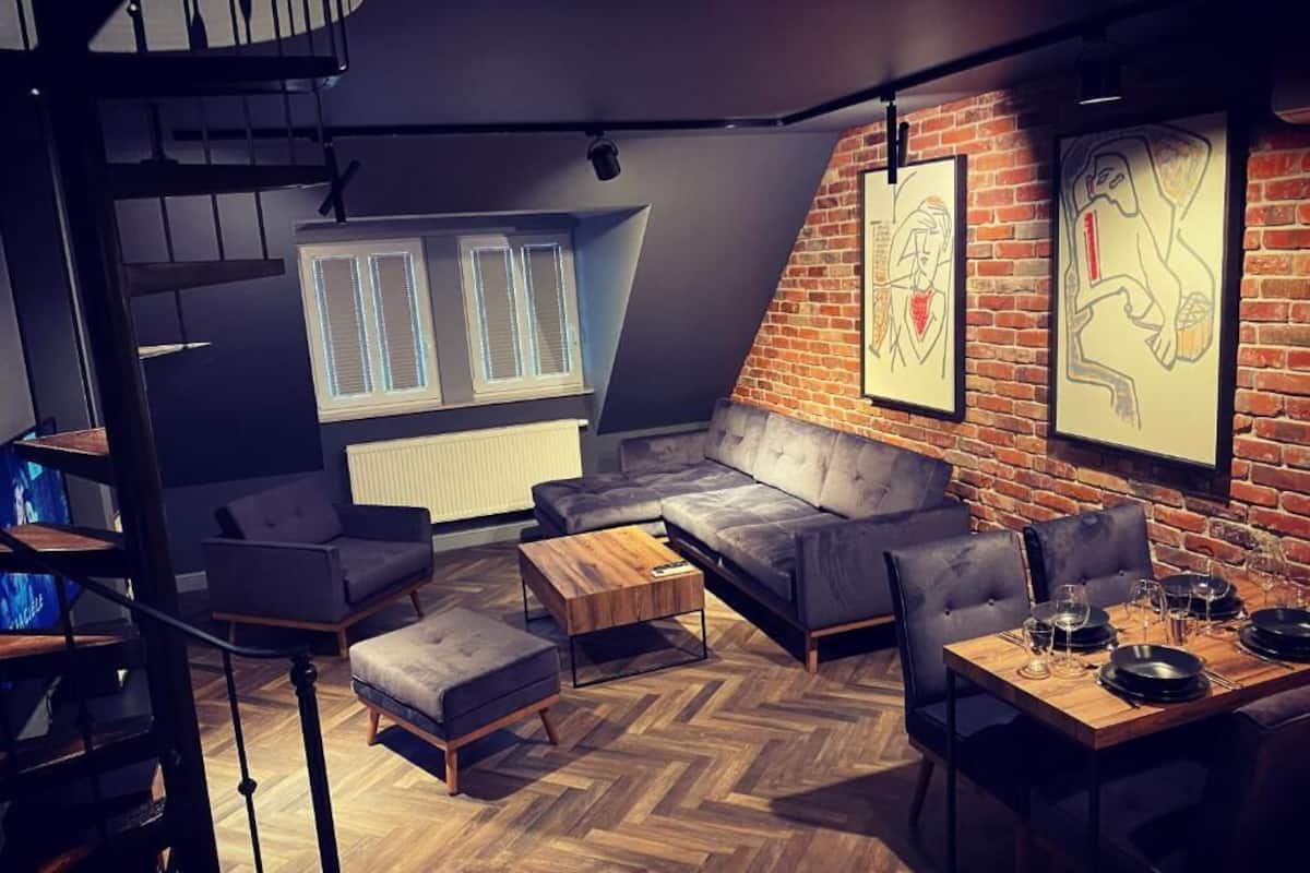 Una sala de estar moderna con piso de espiga, un sofá gris, una mesa de centro de madera y un comedor con una mesa preparada para cuatro.