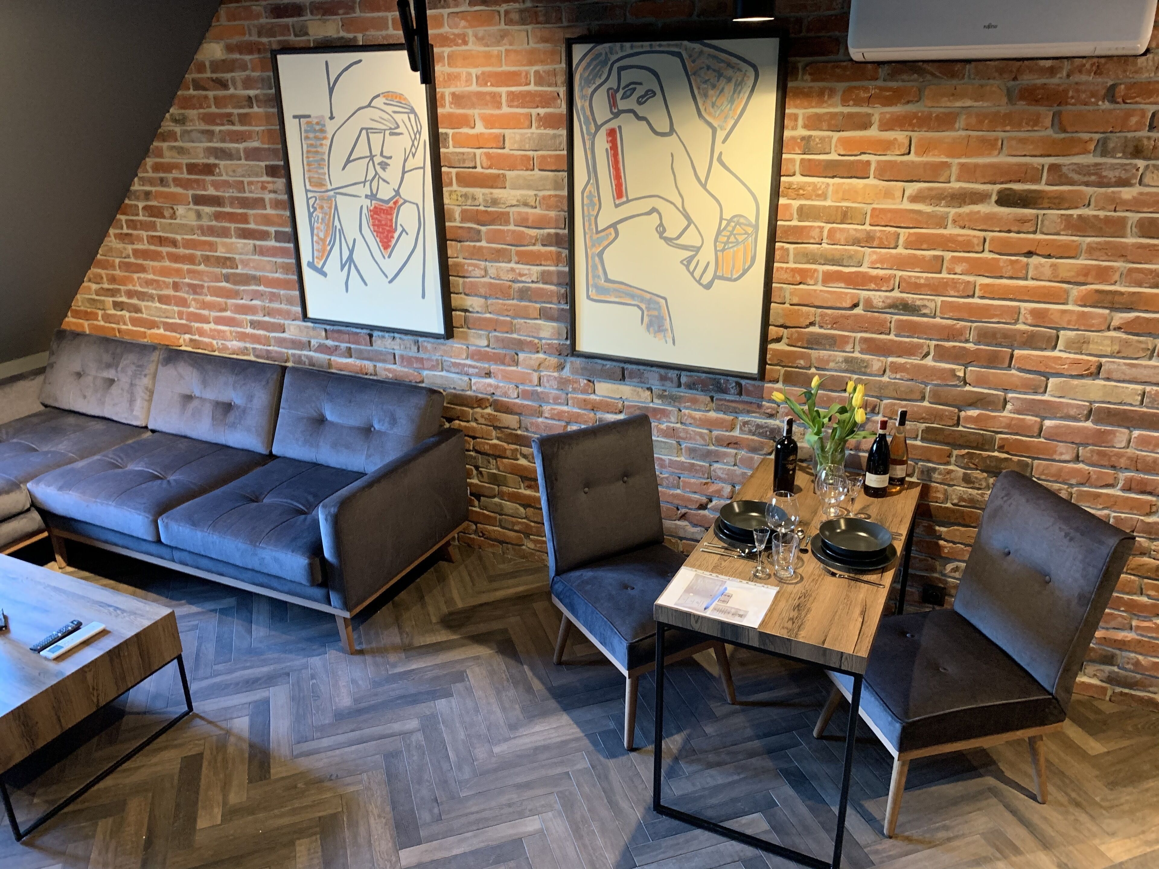 Un interior moderno con pared de ladrillo, un sofá, una mesa de comedor con sillas y obras de arte.