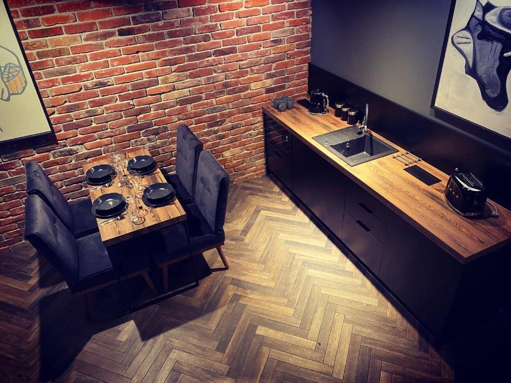A compact kitchen with a herringbone-patterned wooden floor, a brick wall, and a modern black countertop.