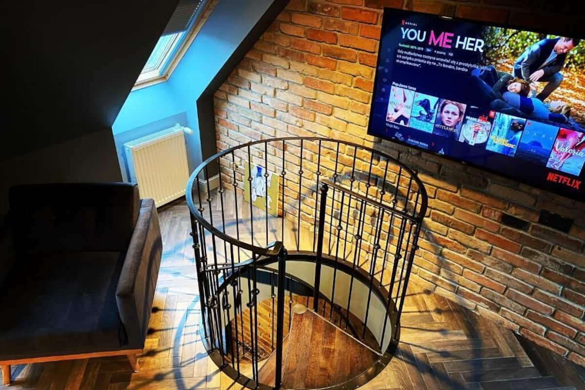 Una habitación con suelo de madera en patrón de espiga, una escalera en espiral de metal negro y una pared de ladrillo.