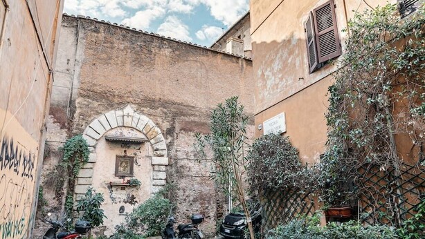 A narrow alley with a rustic building, a small archway, and parked scooters. - Enchanting studio apartment in Trastevere (Roma)