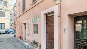 A narrow cobblestone street with a pink building featuring a wooden door and a window. - Enchanting studio apartment in Trastevere (Roma)