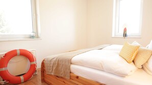 A bedroom with a wooden bed, white bedding, a life preserver, and a window with a view of trees.