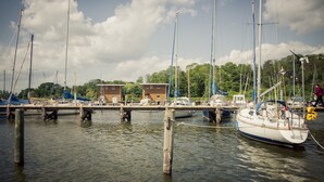 A marina with several boats docked at wooden piers, surrounded by buildings and greenery.