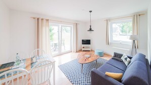 A living room with a sofa, a coffee table, a TV, and a dining area with chairs and a table.