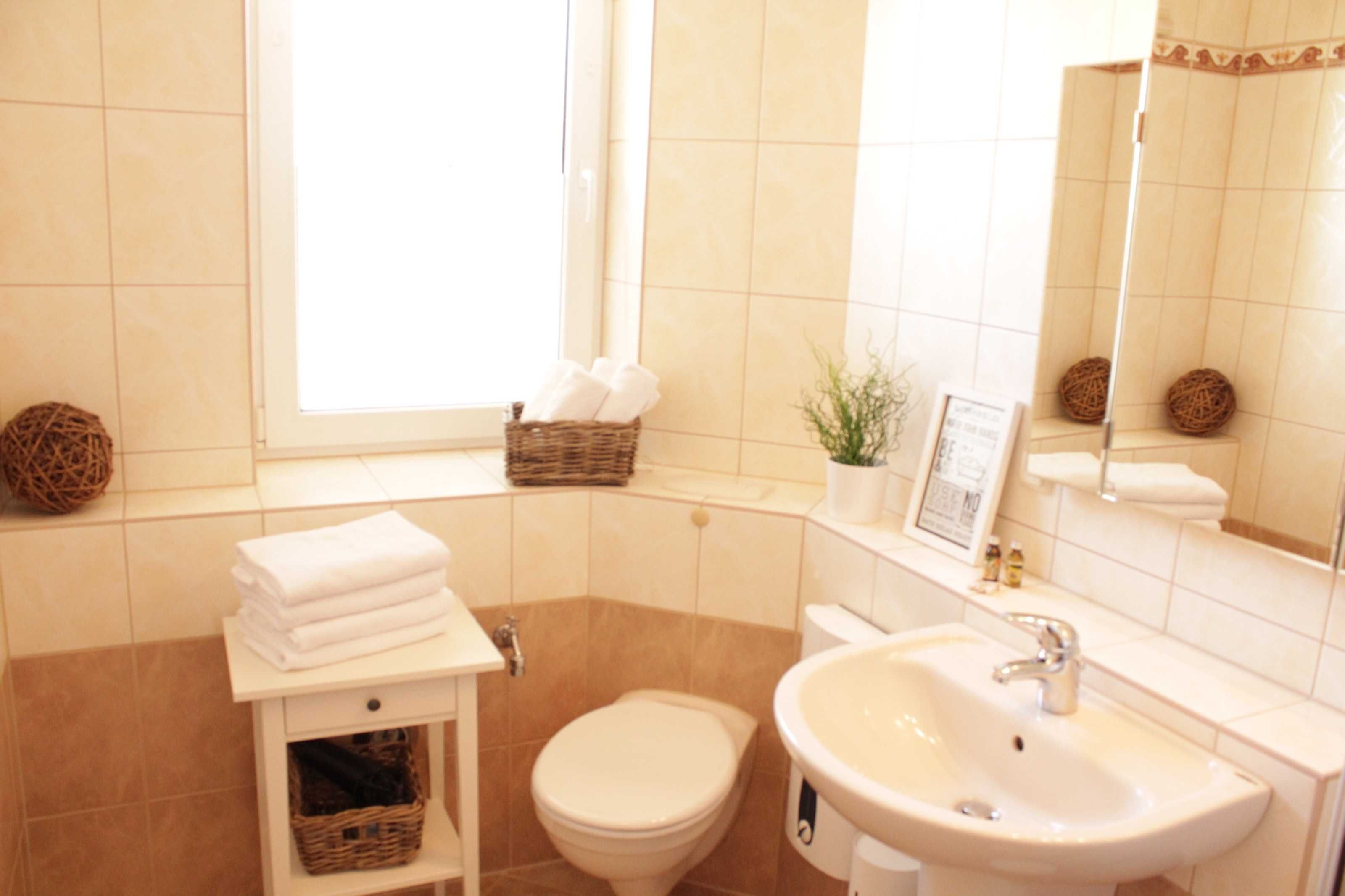 A bathroom with a toilet, sink, and a window with a basket of towels on the windowsill.
