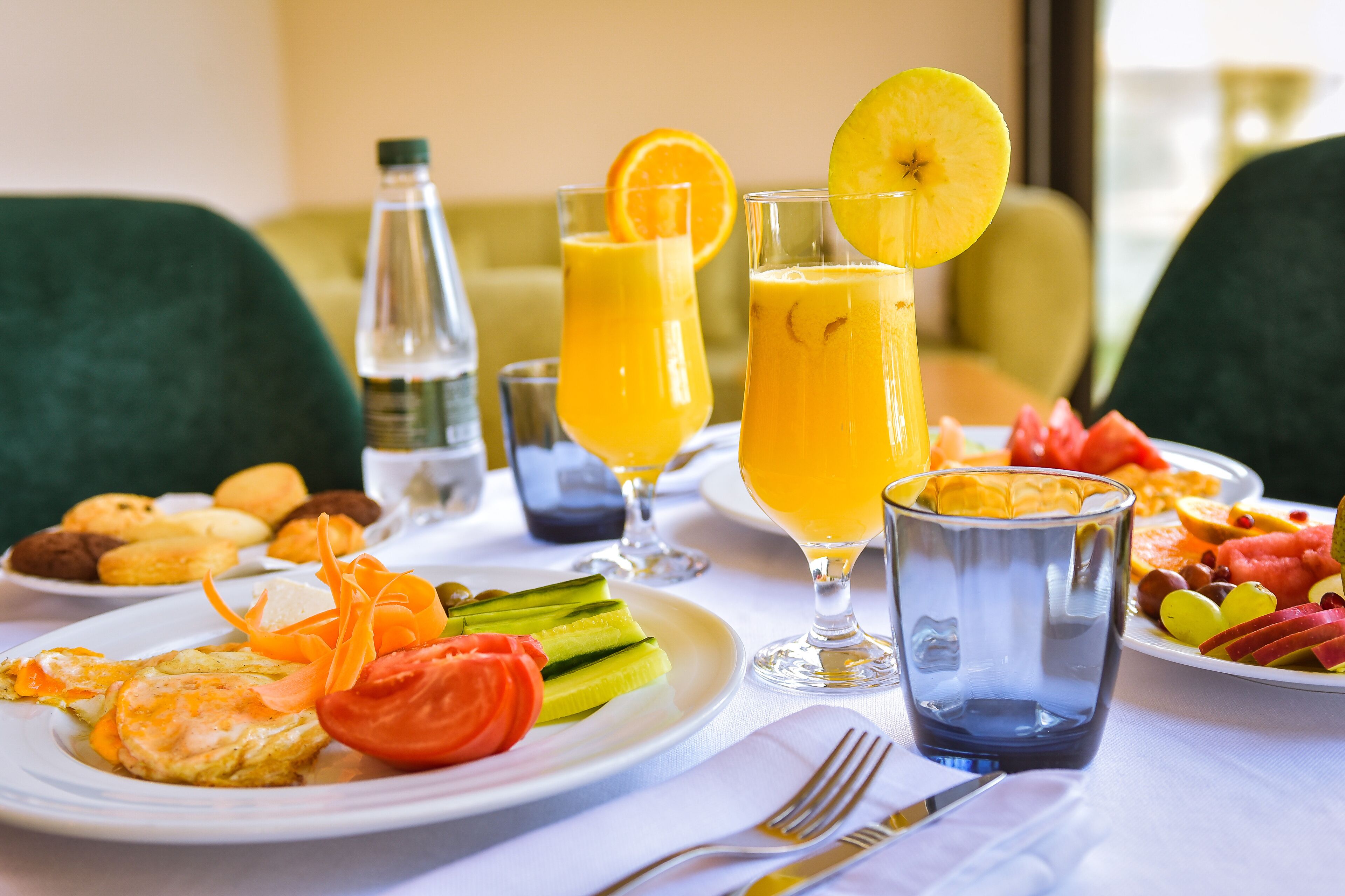 A breakfast setting with plates of food, glasses of orange juice, and a bottle of water.